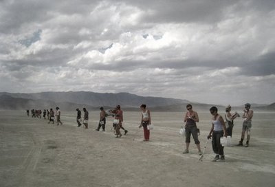 Burners in a line on playa during a line sweep to pick up trash. 
