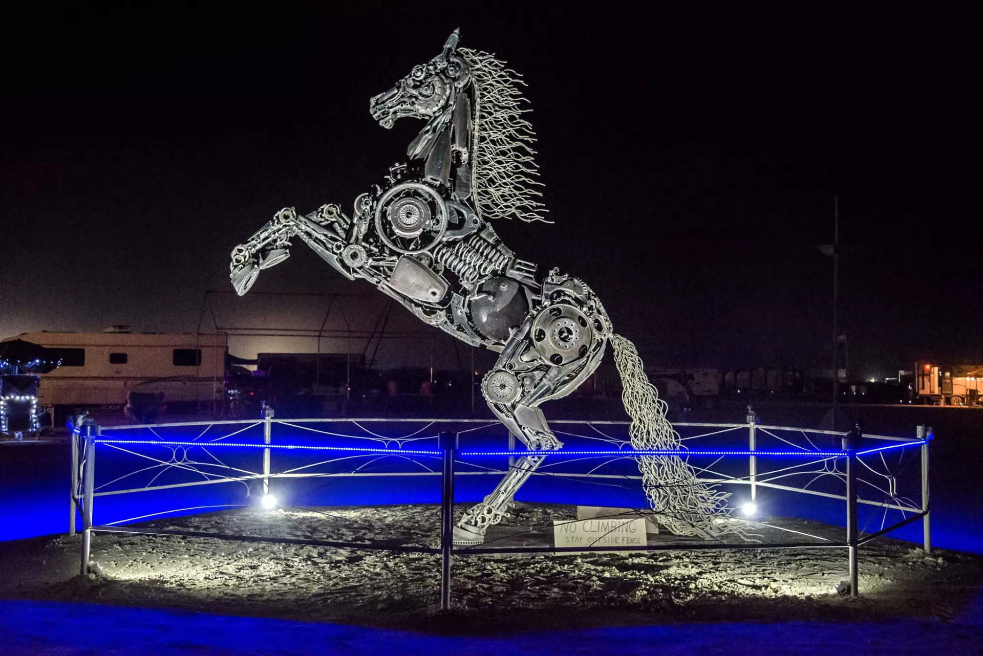 Large metal rearing horse sculpture made of salvaged metal parts illuminated by a ring of blue LEDs at night on playa 