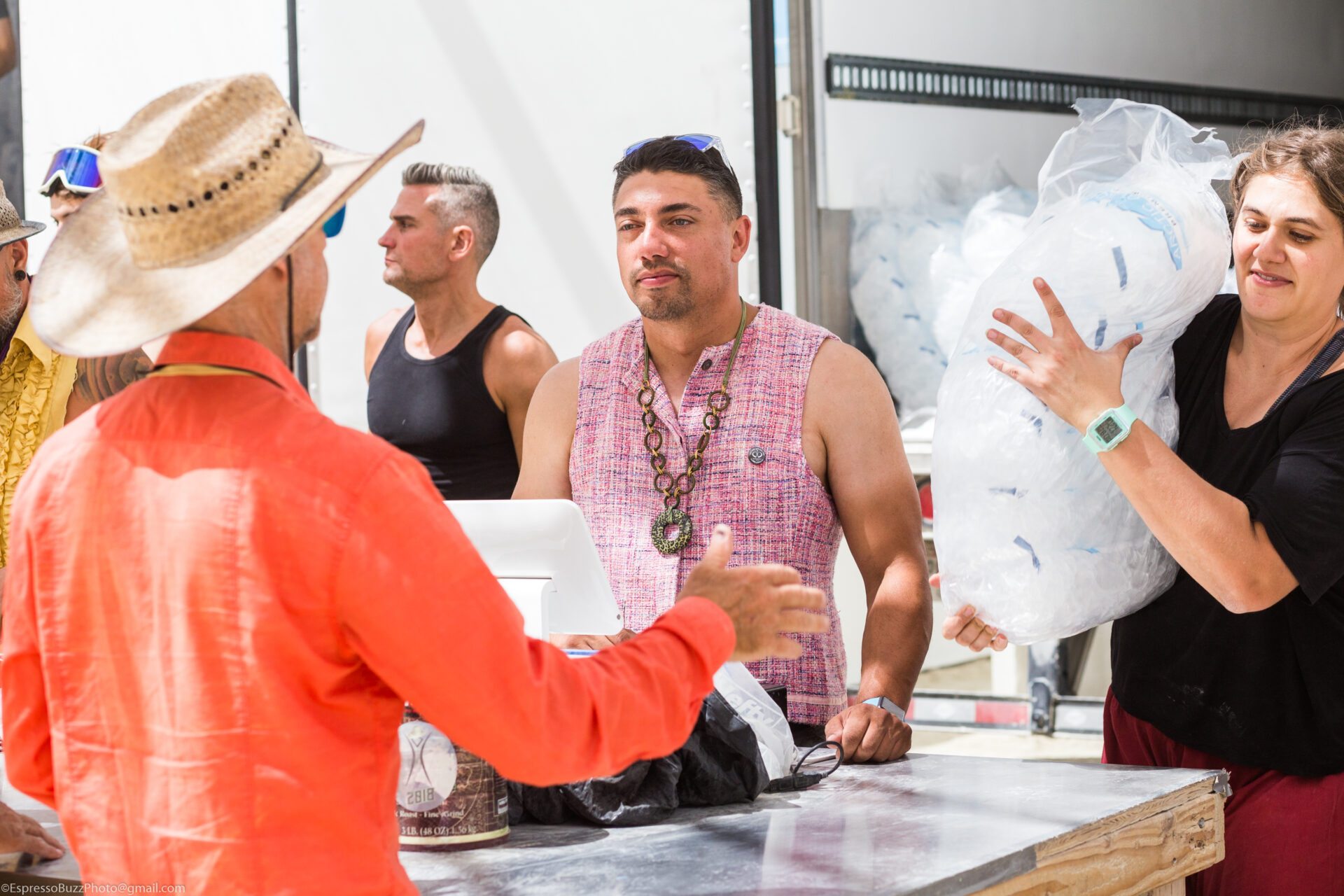 A woman carries bags of ice while a man takes an order at a cash register.