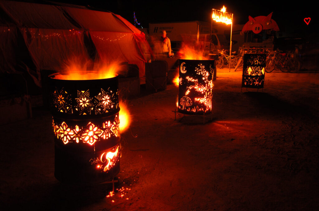 Three burn barrels with intricate patterns cut into the sides in front of a large tent. 