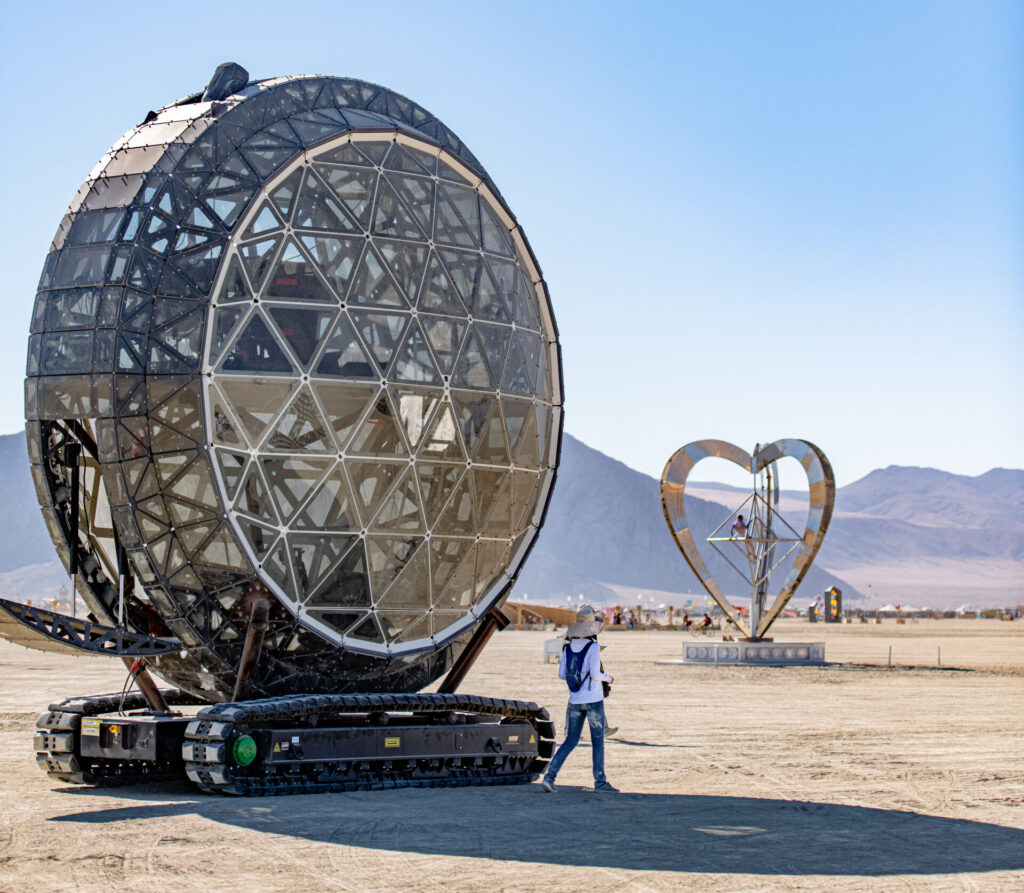 A disc-shaped mutant vehicle on tank tracks in front of a heart-shaped sculpture.