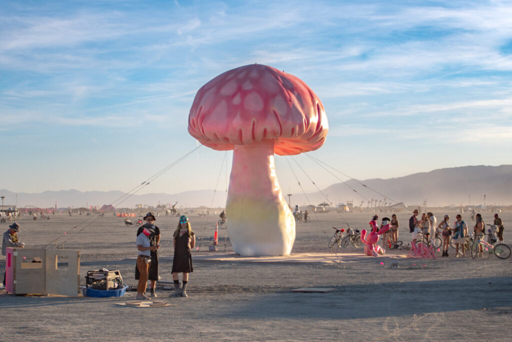 A 30-foot pink and yellow spotted mushroom sculpture on playa during daytime.