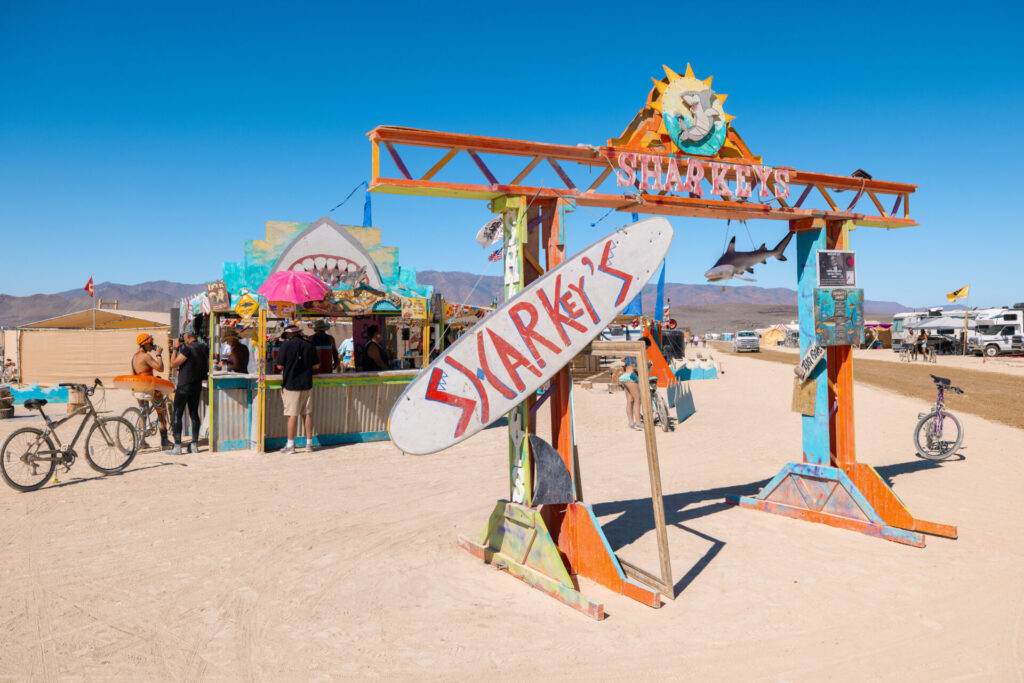 Sharky's theme camp sign in the shape of a surfboard.