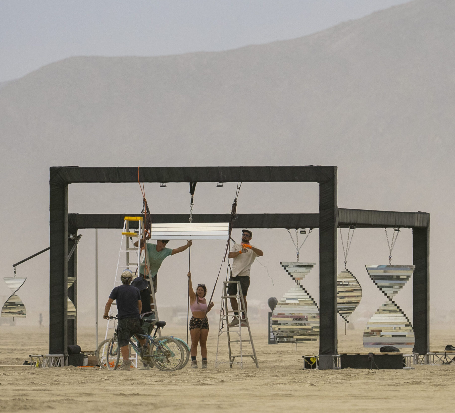 People on ladders hanging mirrored helix from a support beam.