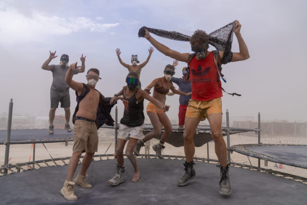 A group of burners jumping on a trampoline in a dust storm 
