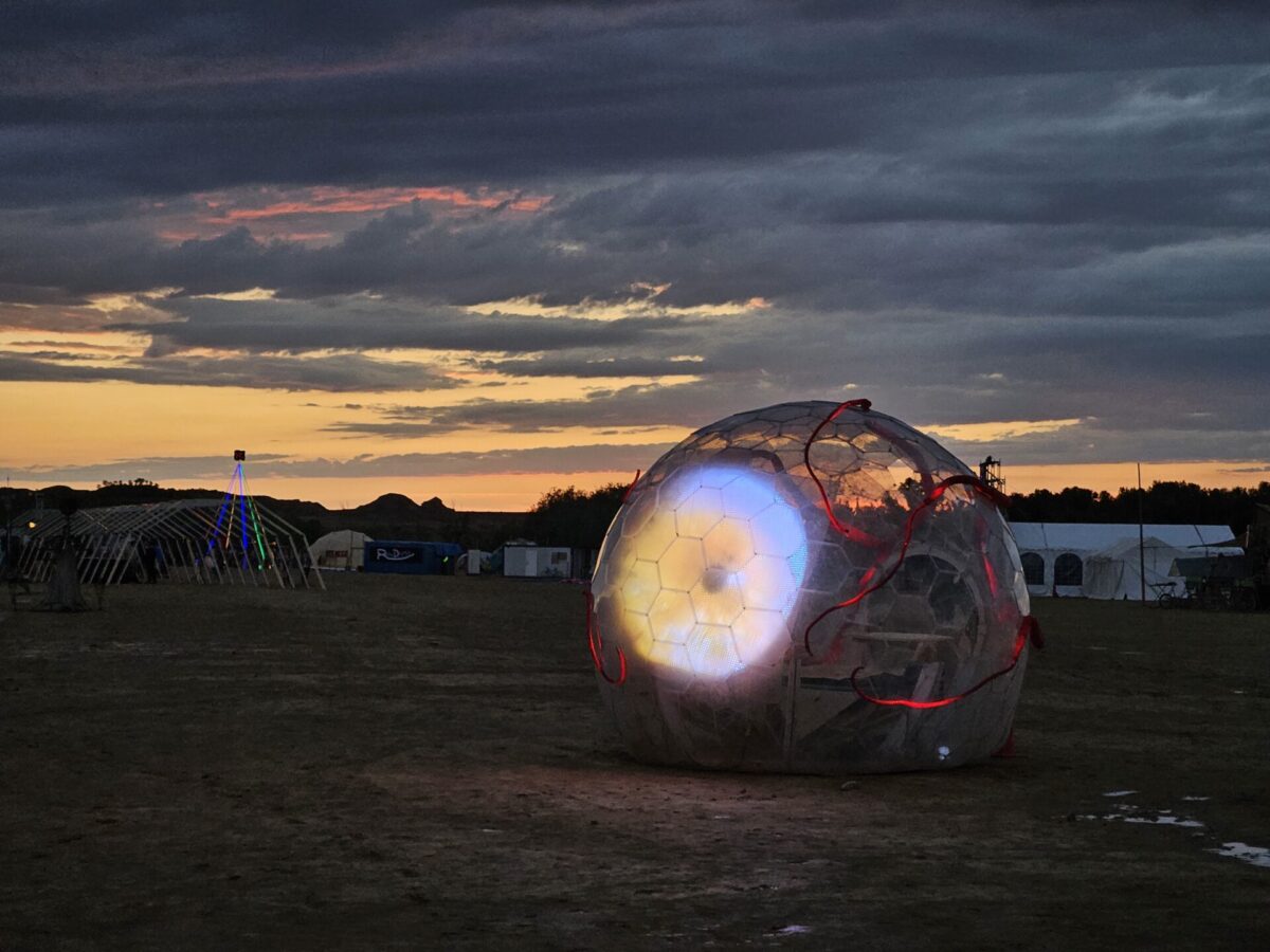 An illuminated eye at the ege of a camping area in a forest.