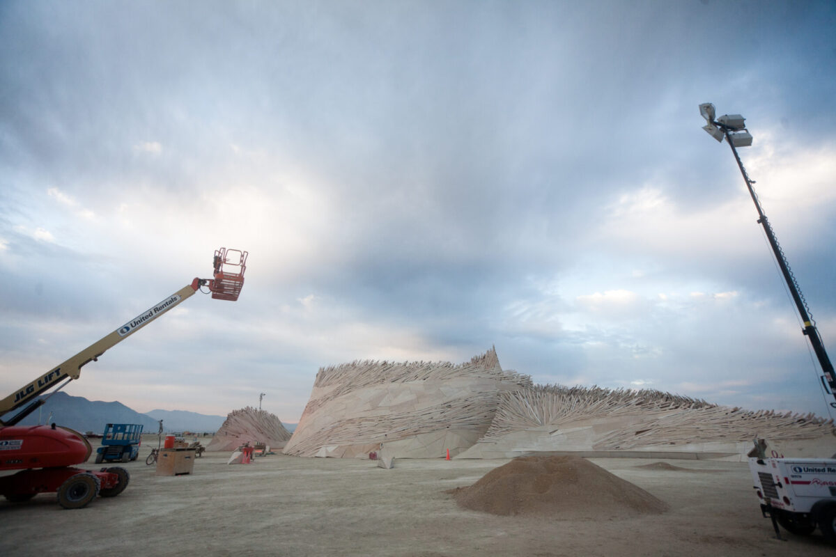 A worksite with cherry-picker and lighting over an organic shaped structure