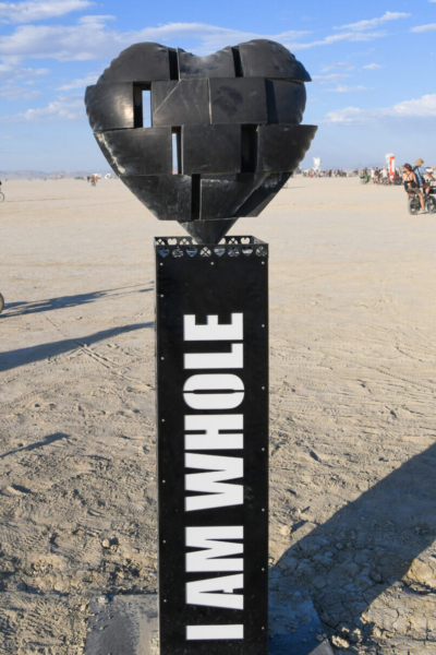 Black heart made of metal sections with gaps between on a pedestal that says "I am whole"