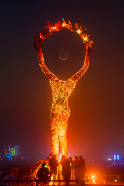 A headless female figure with arms raised in a circle above het, with crescent moon in the the circle of her arms.