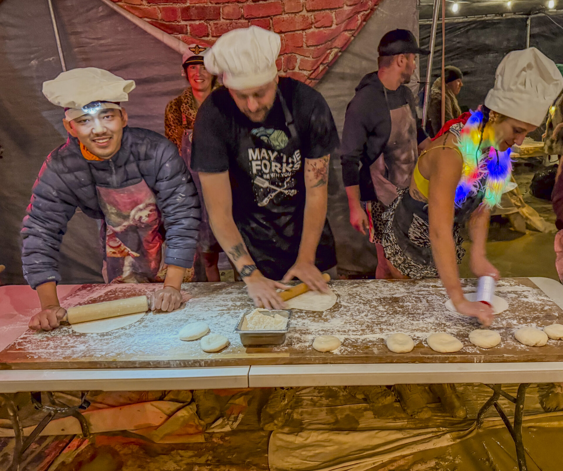 People rolling pizza dough under a shade structure