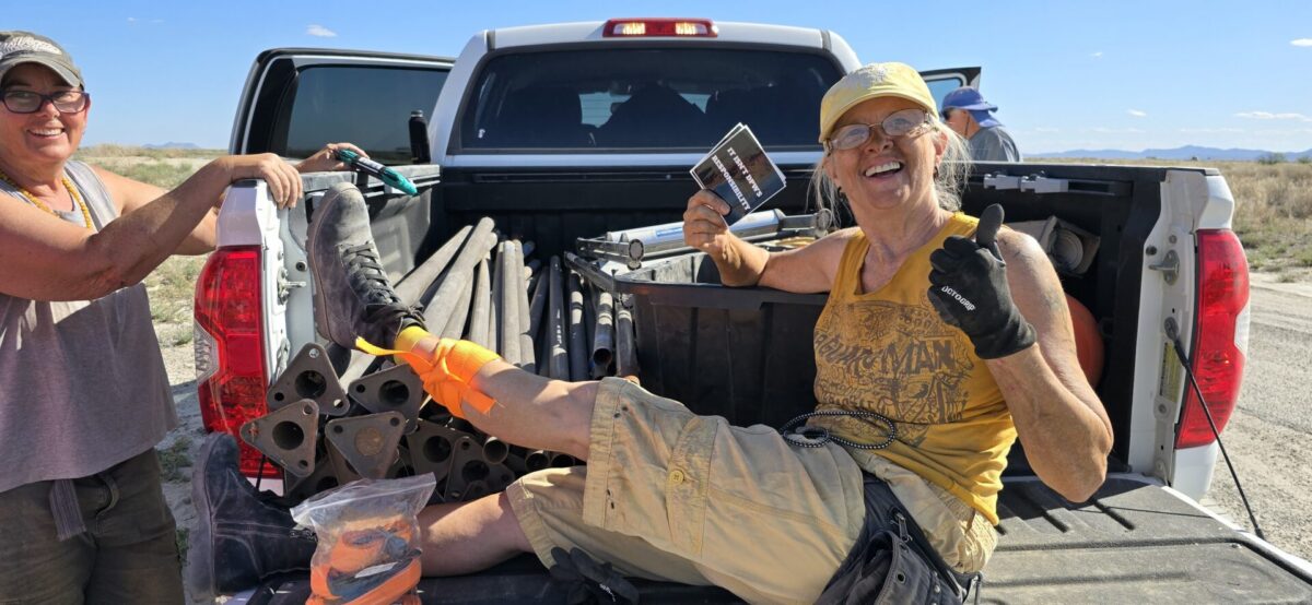 A smiling woman on the tail gate of a pickup truck holds up a sticker that reads, "It isn't DPW's Responsibility"
