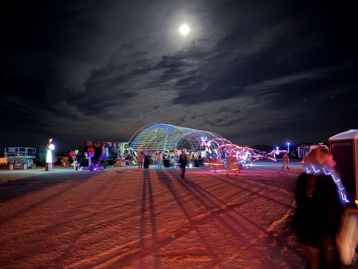 An arched tunnel of LED lights under a full moon