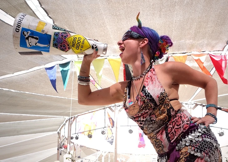 A colorfully-dressed woman calls out through a megaphone decorated with stickers.